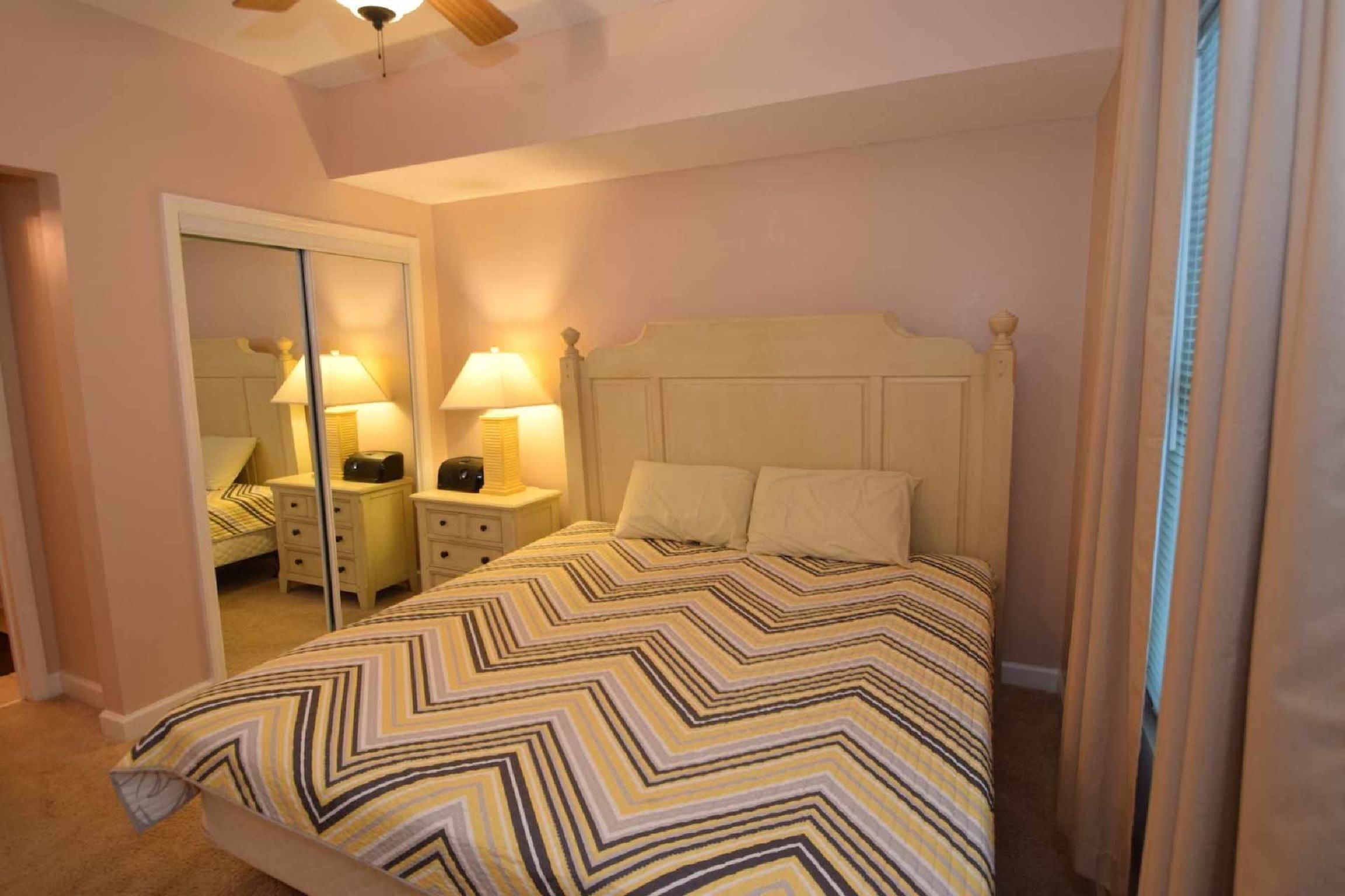 A bedroom with a bed, nightstands, lamps, a mirror, and a ceiling fan.