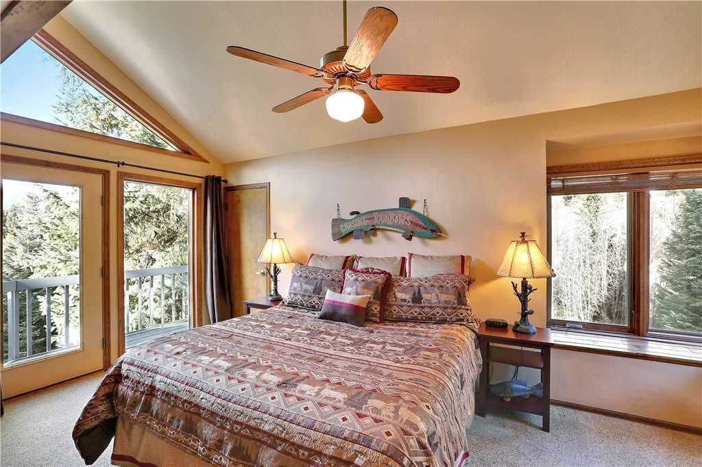 A bedroom with a large bed, two bedside lamps, a ceiling fan, and a window with a view of trees.