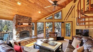 Una sala de estar acogedora con chimenea de piedra, sofás de cuero y un ventilador de techo.