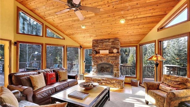 Un salón amplio con chimenea de piedra, sofás de cuero y ventanas grandes que ofrecen vistas al bosque.