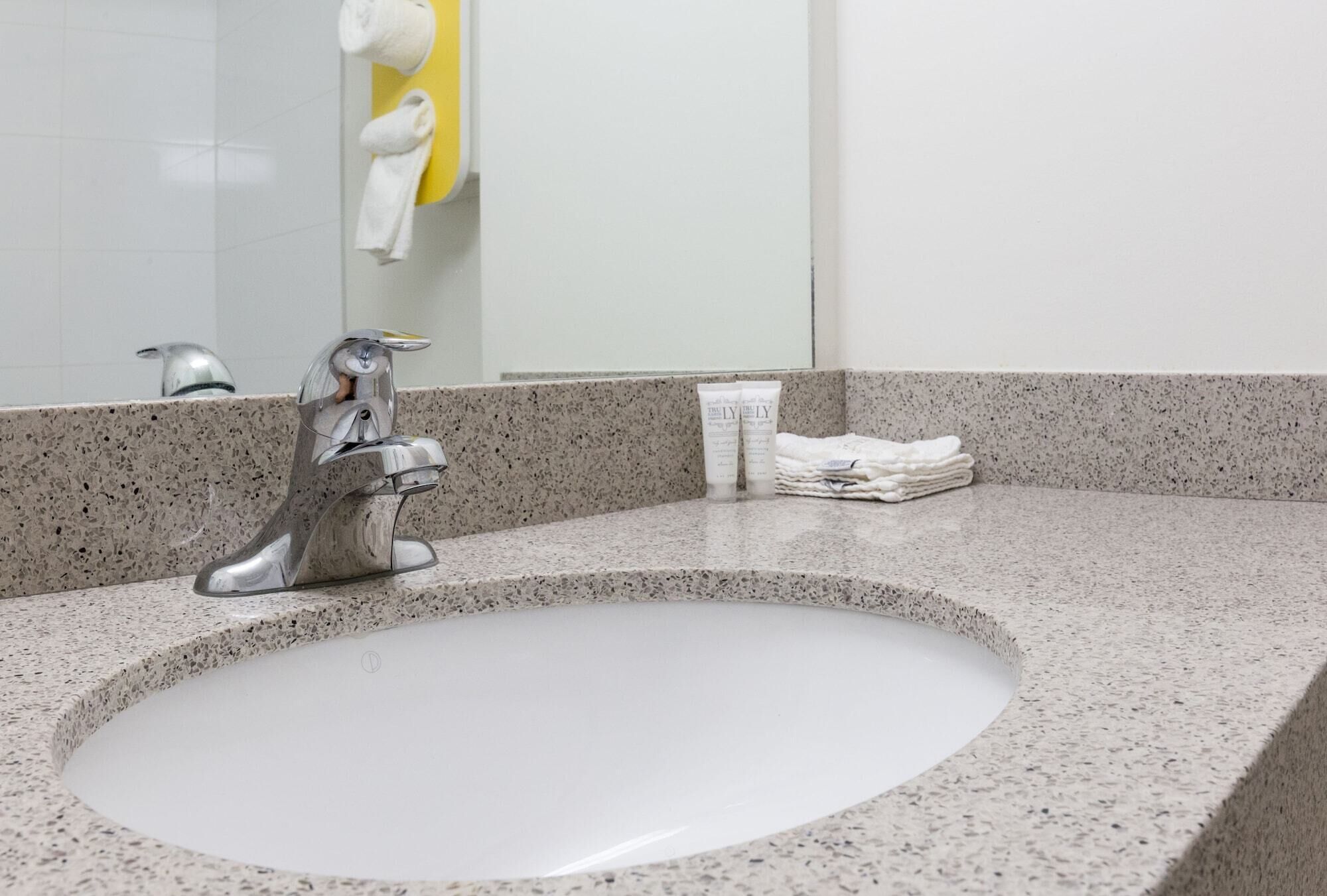 A bathroom sink with a modern faucet, a mirror, and a towel dispenser.