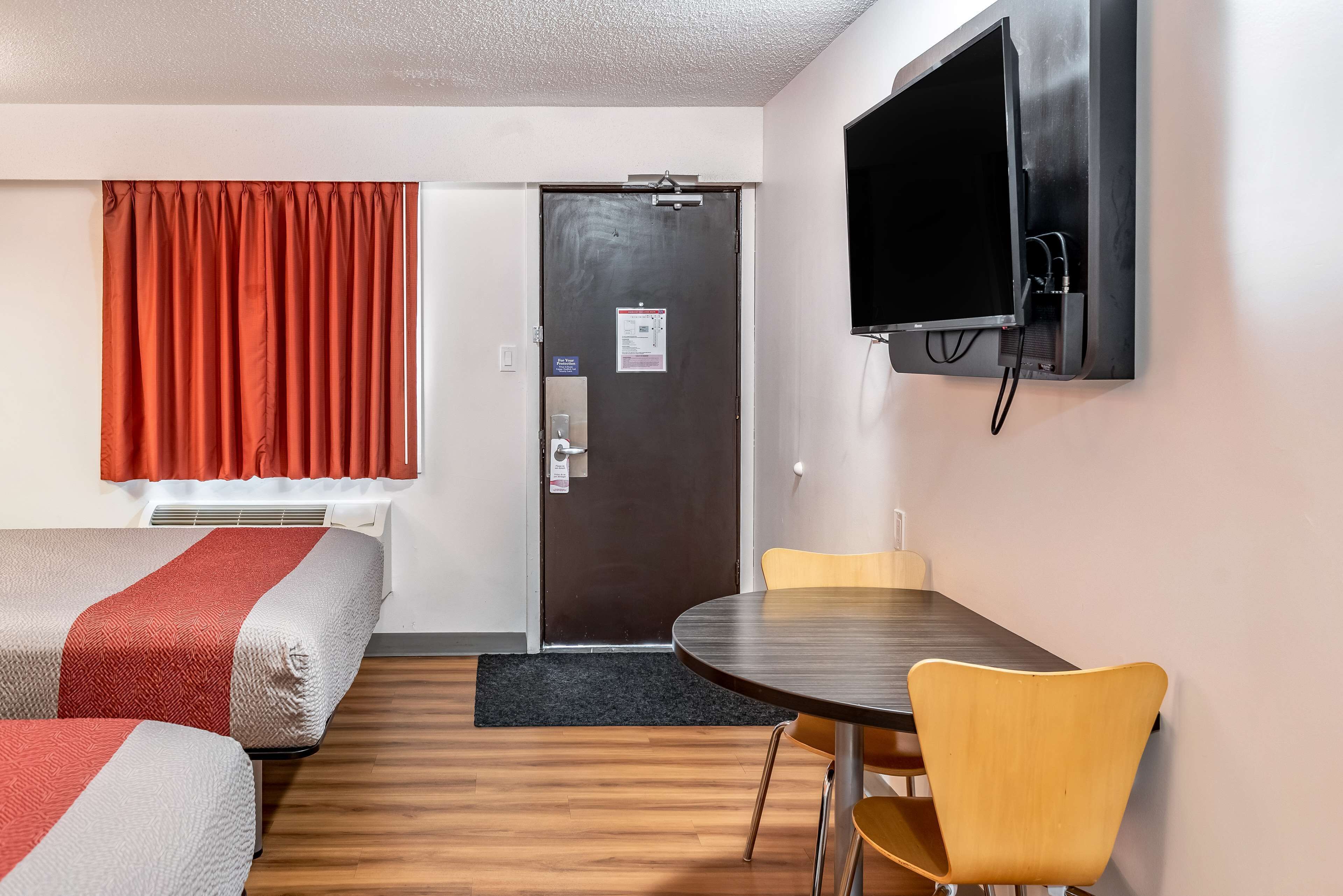 A hotel room with two beds, a dining table, a TV, and a door.