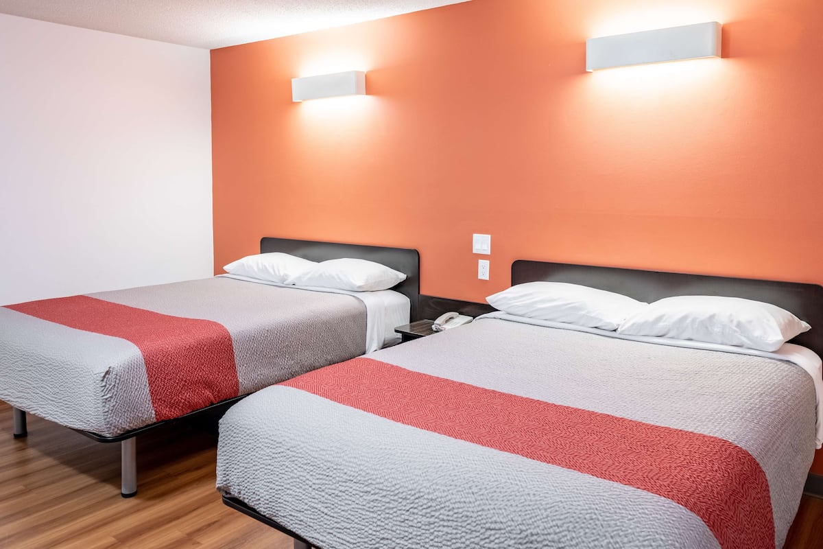 Two beds with white and red bedding, a wooden floor, and a wall-mounted light fixture.