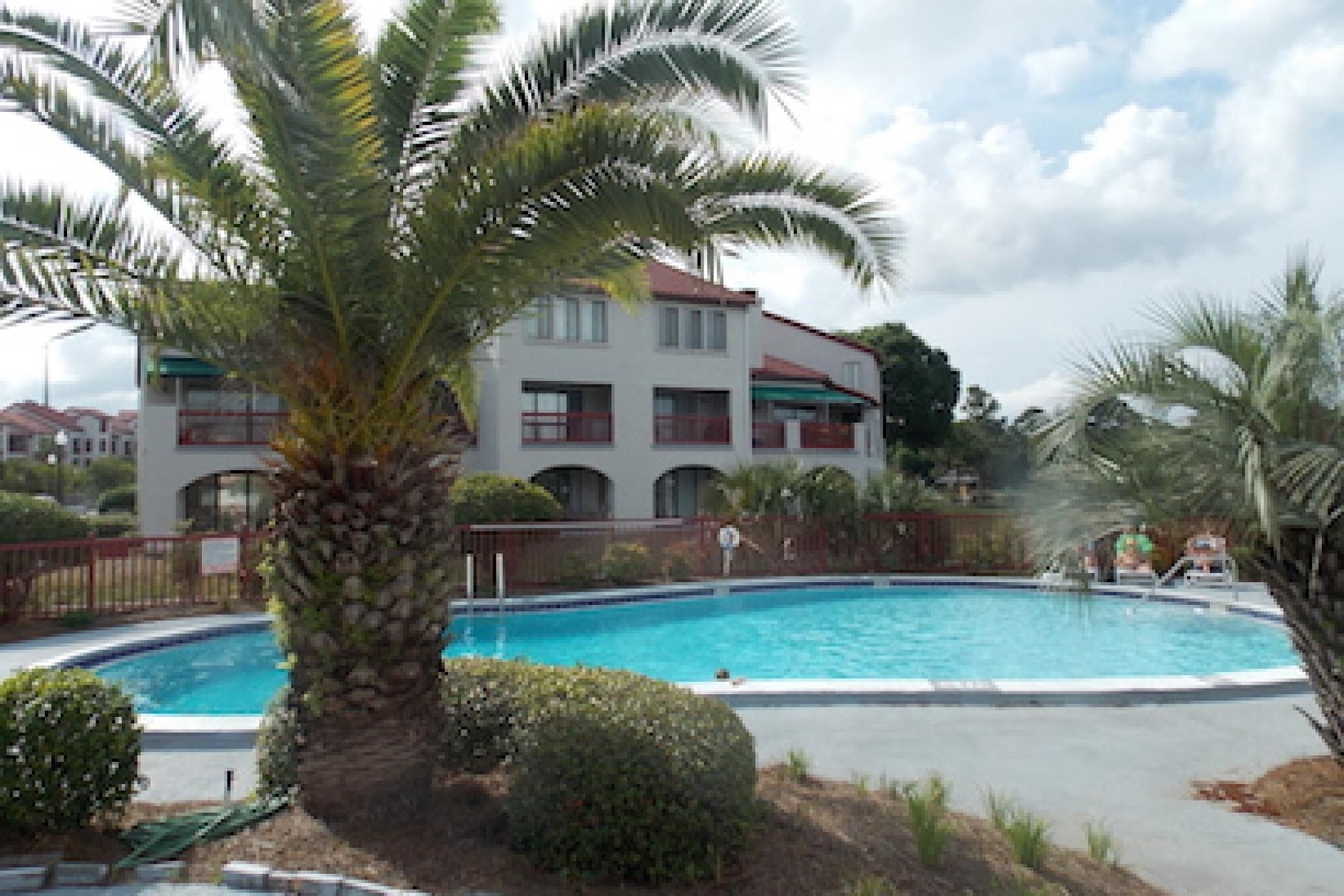 Une piscine entourée de palmiers et un bâtiment doté de balcons.