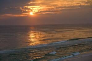 A sunset over the ocean with waves approaching the shore.