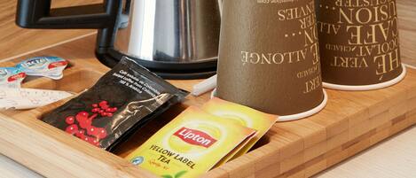 Una tetera de acero inoxidable, dos vasos desechables, un sobre de café instantáneo y un sobre de té Lipton sobre una bandeja de madera.