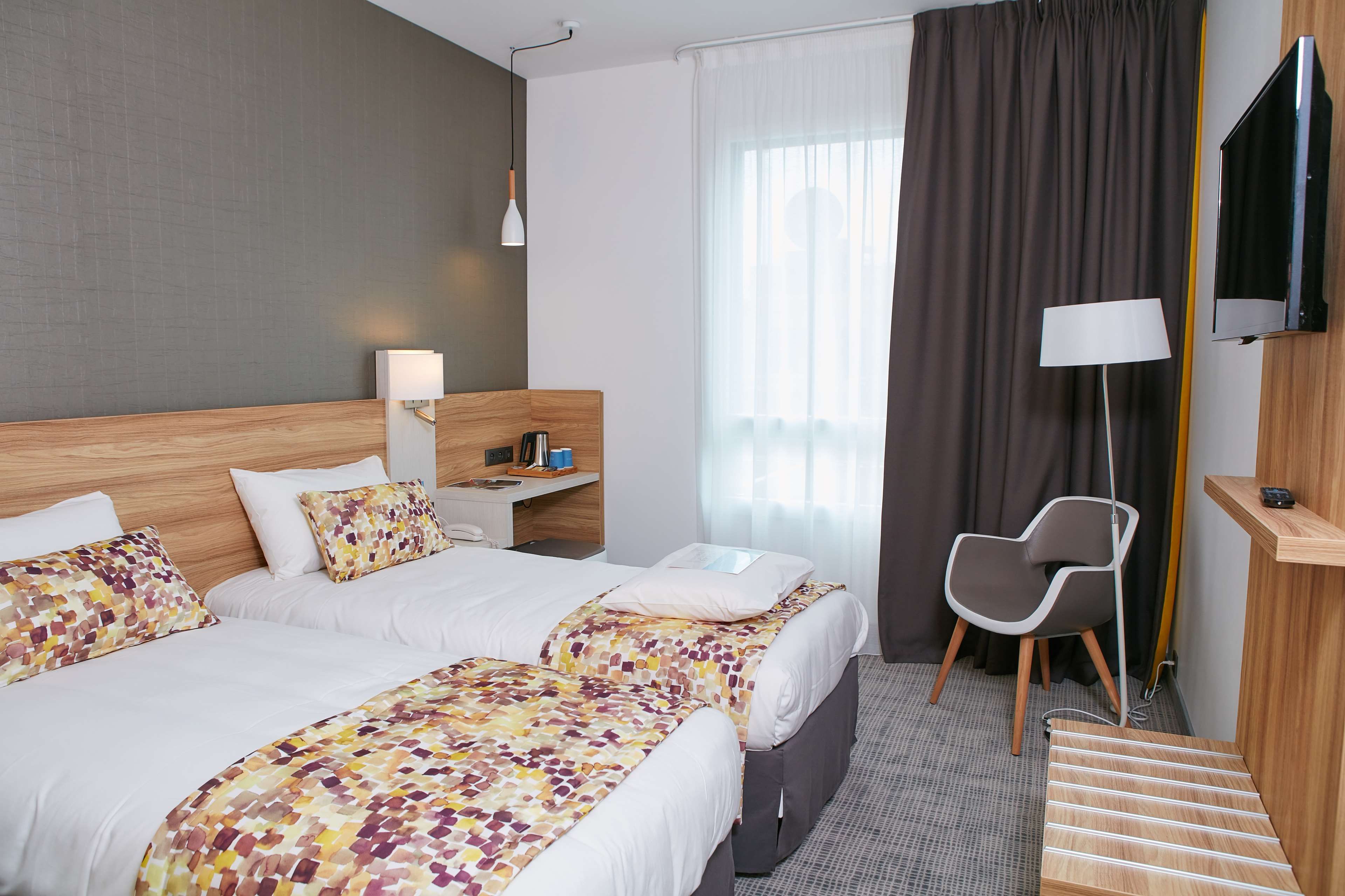 Une chambre d’hôtel avec deux lits, un bureau, une chaise, une télévision et une fenêtre avec des rideaux.