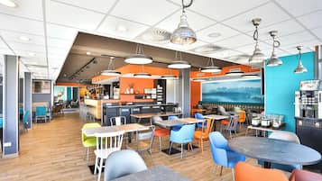 Un café moderne doté de plusieurs espaces de détente, notamment des tables et des chaises, ainsi que d’un bar équipé d’une machine à café.