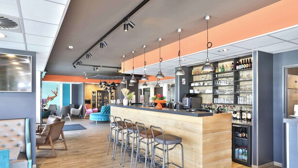 Un espace bar moderne avec un comptoir en bois, des tabourets en métal et un présentoir réfrigéré.