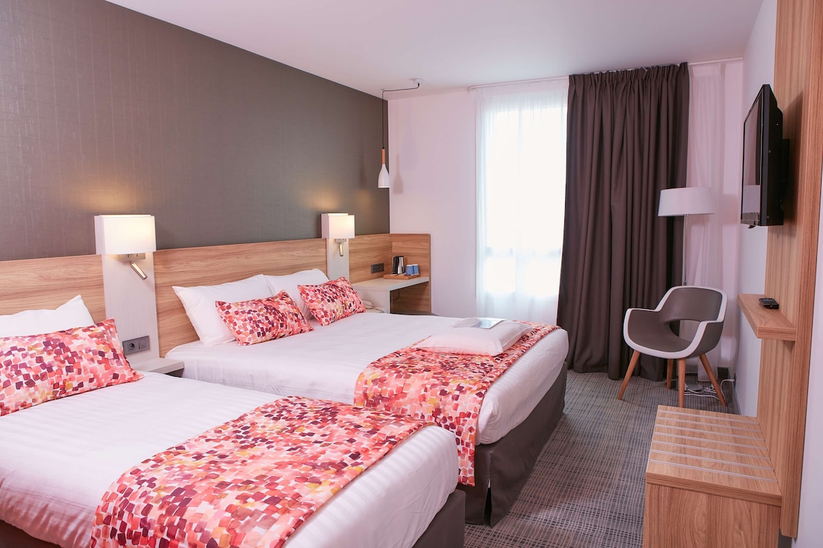 A hotel room with two beds, a desk, a chair, a TV, and a window with curtains.