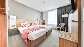 A hotel room with a large bed, a desk, a chair, a TV, and a window with curtains.