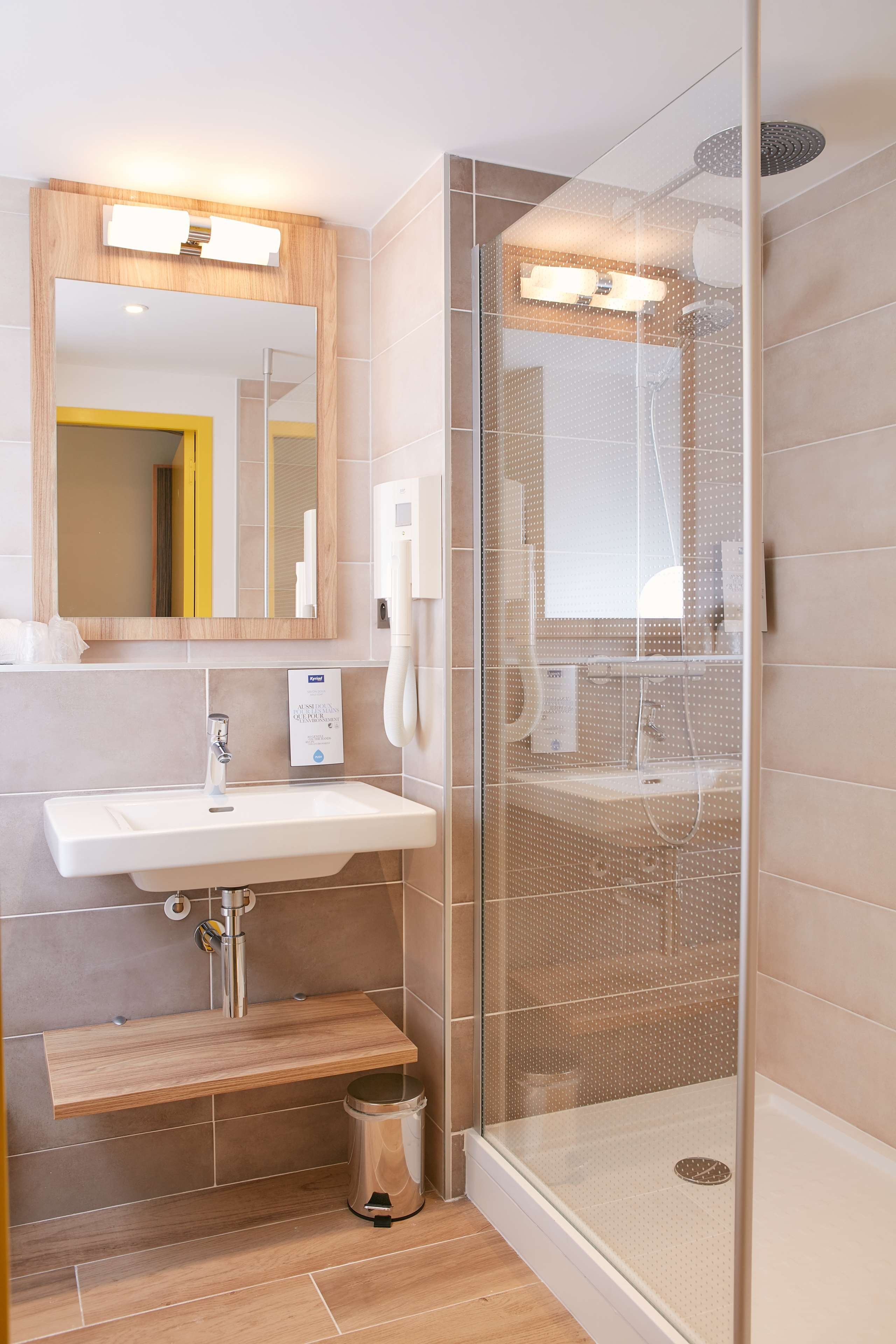 A modern bathroom with a glass shower enclosure, a sink with a mirror, and a wooden bench.