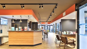 Un intérieur moderne avec un comptoir d’accueil en bois, des tabourets de bar et un espace salon comprenant des tables et des chaises.