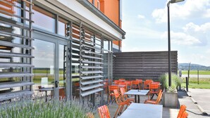 Un espace extérieur aménagé avec des tables et des chaises, une terrasse en bois et une vue sur un bâtiment doté de grandes fenêtres.
