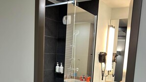 Une salle de bain moderne avec une douche à parois de verre, un lavabo avec un miroir et un sèche-cheveux fixé au mur.