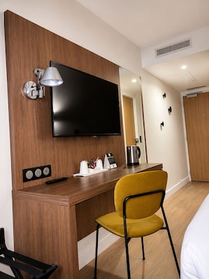 Habitación de hotel con un escritorio de madera, un televisor de pantalla plana, una silla amarilla, una cafetera y una cama.