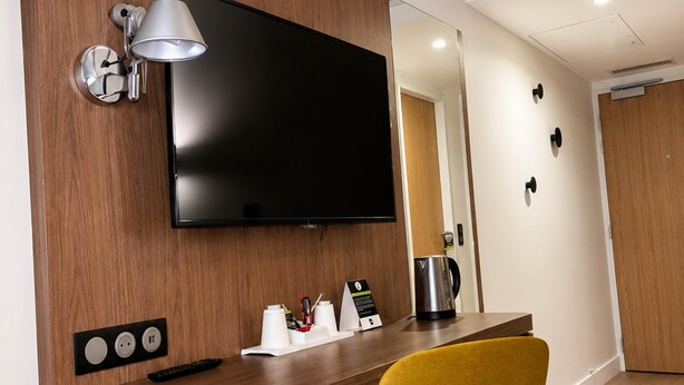Une chambre d’hôtel avec un bureau en bois, un téléviseur à écran plat, une machine à café et une chaise jaune.