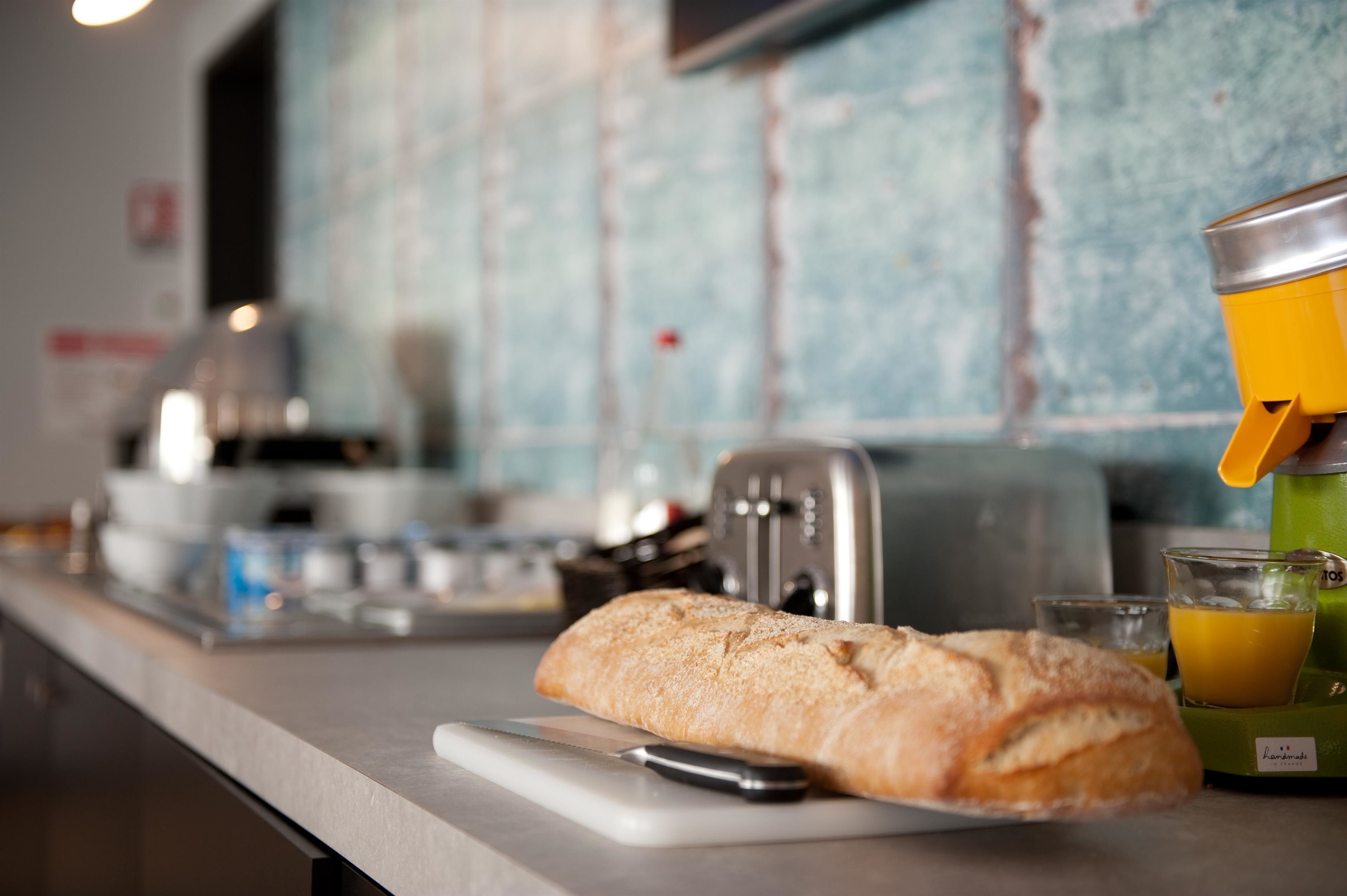 A kitchen counter with a loaf of bread, a toaster, and a glass of orange juice.