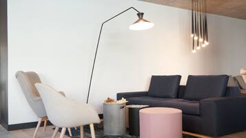 A modern living room with a dark grey sofa, two armchairs, a floor lamp, and a round table with a chess set.