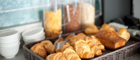 Un bufé de desayuno con cruasanes, pan y tazas de café.