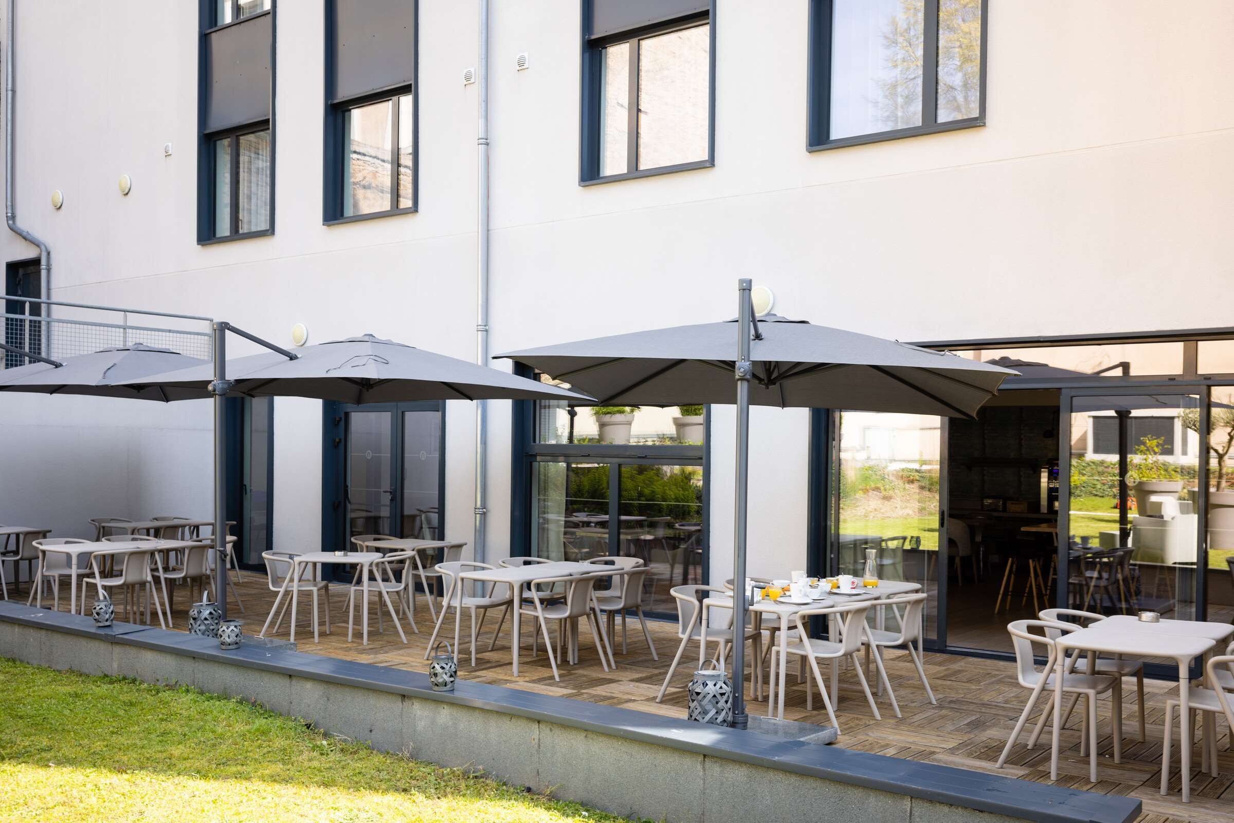 Un patio al aire libre con mesas, sillas, sombrillas y vistas al interior del edificio.