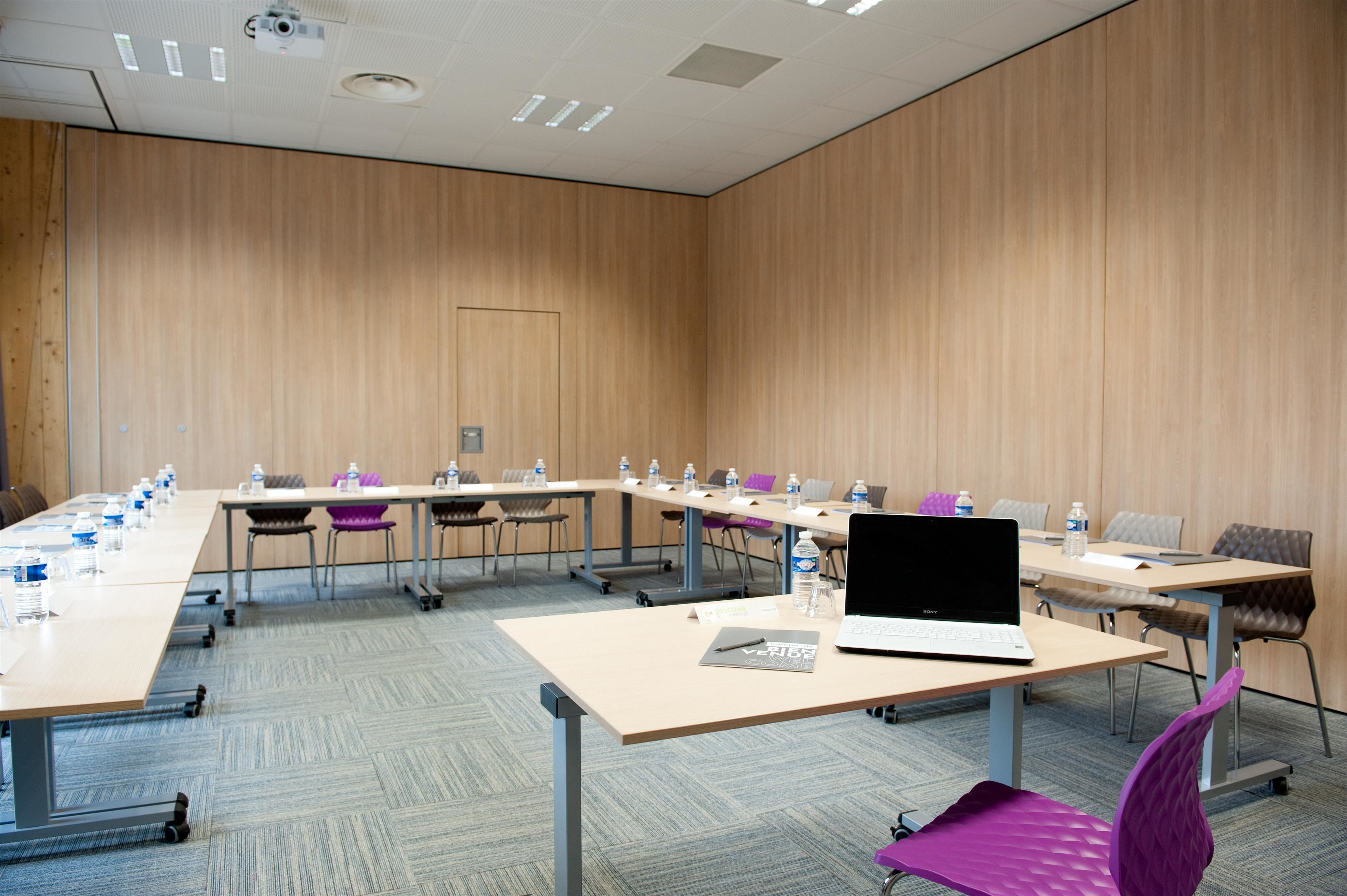 Ein Konferenzraum mit langem Tisch, Stühlen, Laptops, Wasserflaschen und einem Projektor an der Decke.