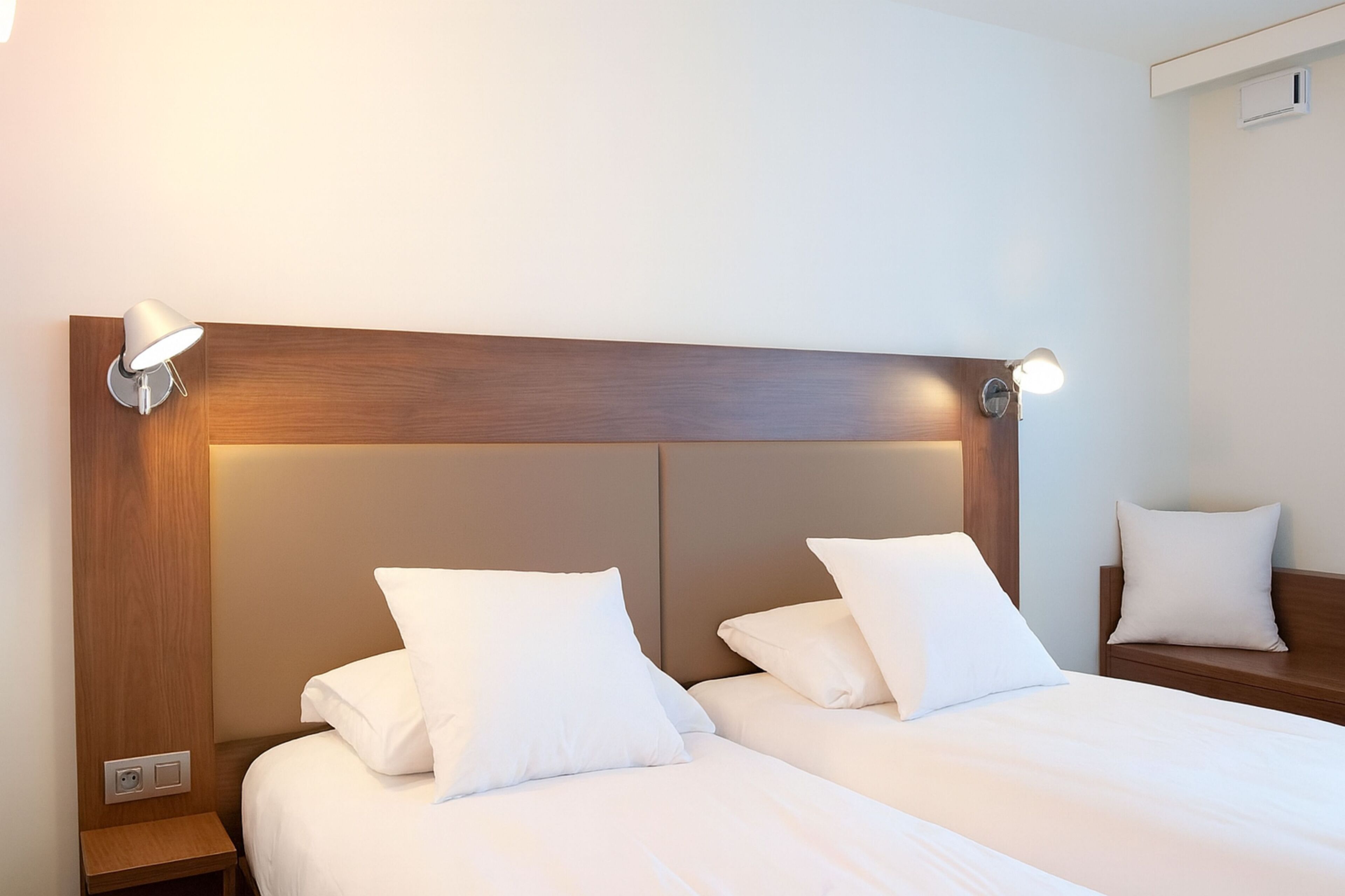 A hotel room with a wooden headboard, two beds with white bedding, and bedside lamps.