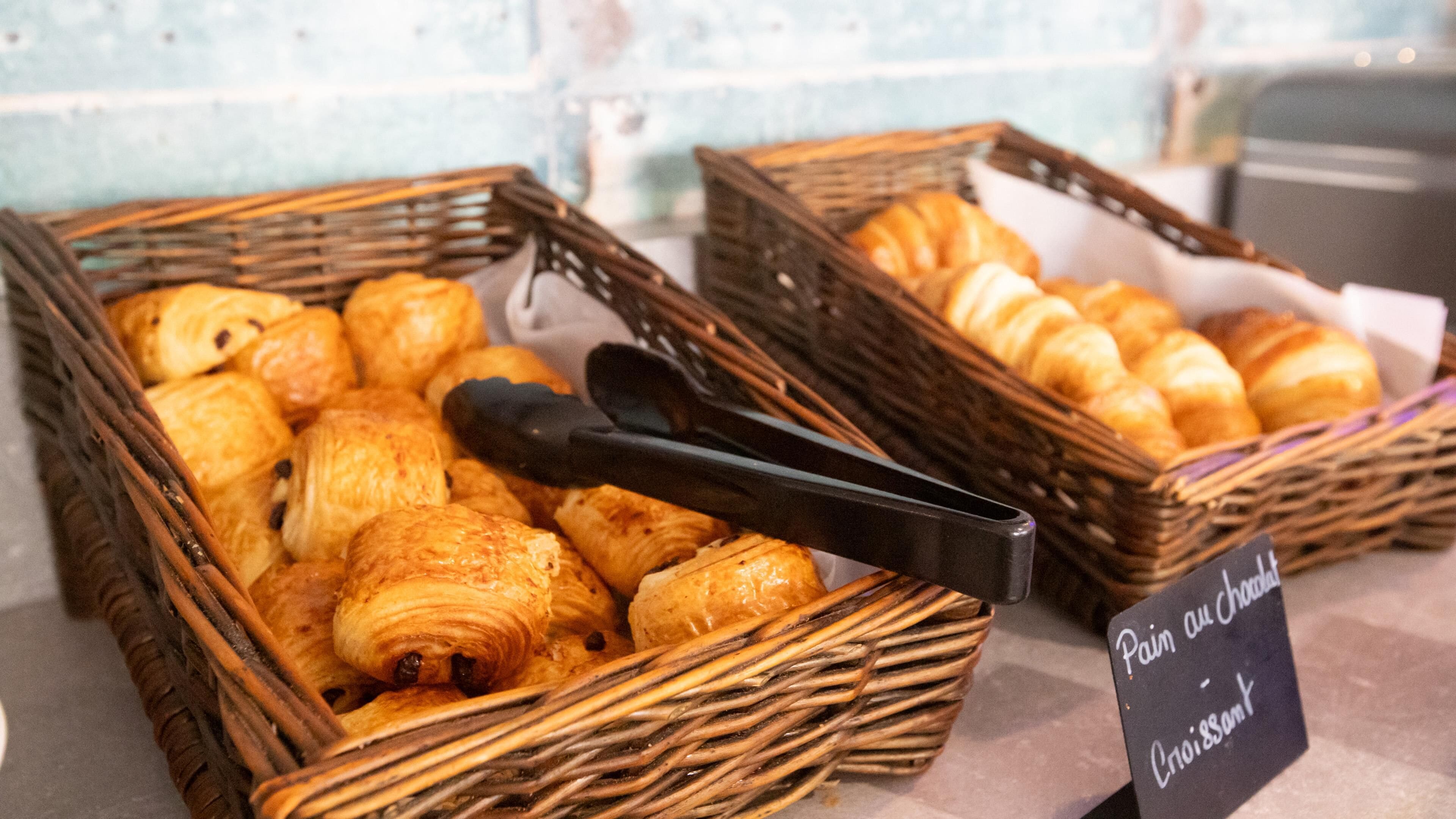 Wicker baskets filled with pastries, including croissants and chocolate-covered items, displayed on a counter with a sign indicating they are available for purchase.