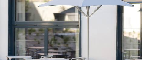 A café with outdoor seating, a large umbrella, and a view through large windows.