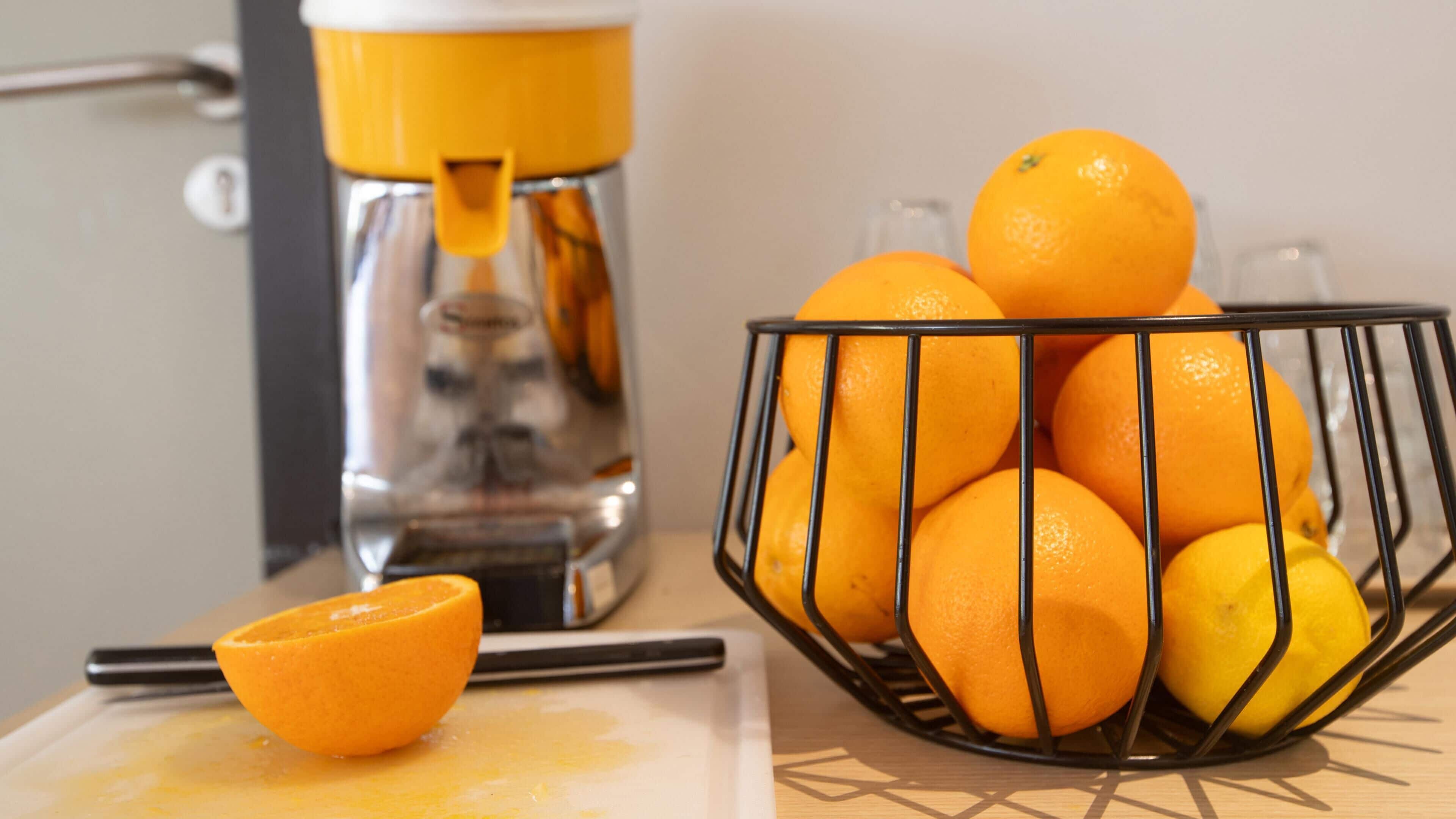 A kitchen counter with a juicer, a bowl of oranges, and a half-cut orange on a cutting board.