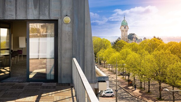 Un edificio moderno con un amplio ventanal y una vista de un edificio histórico con una cúpula verde al fondo.