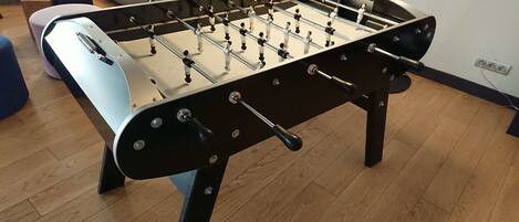 A foosball table in a room with wooden flooring and a sofa in the background.