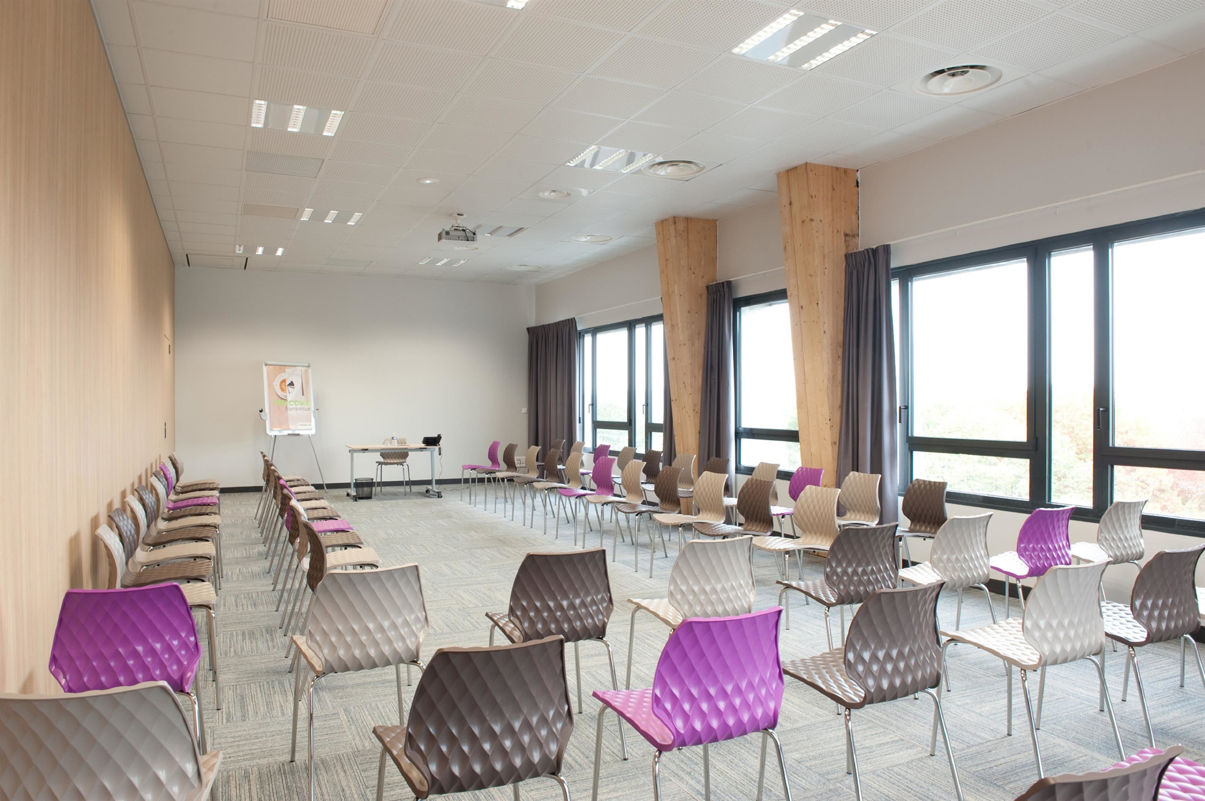 Un salón de conferencias con filas de sillas, ventanas amplias y una pizarra.