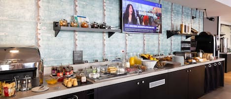 A breakfast bar with a TV displaying a news program, various food items, and condiments.
