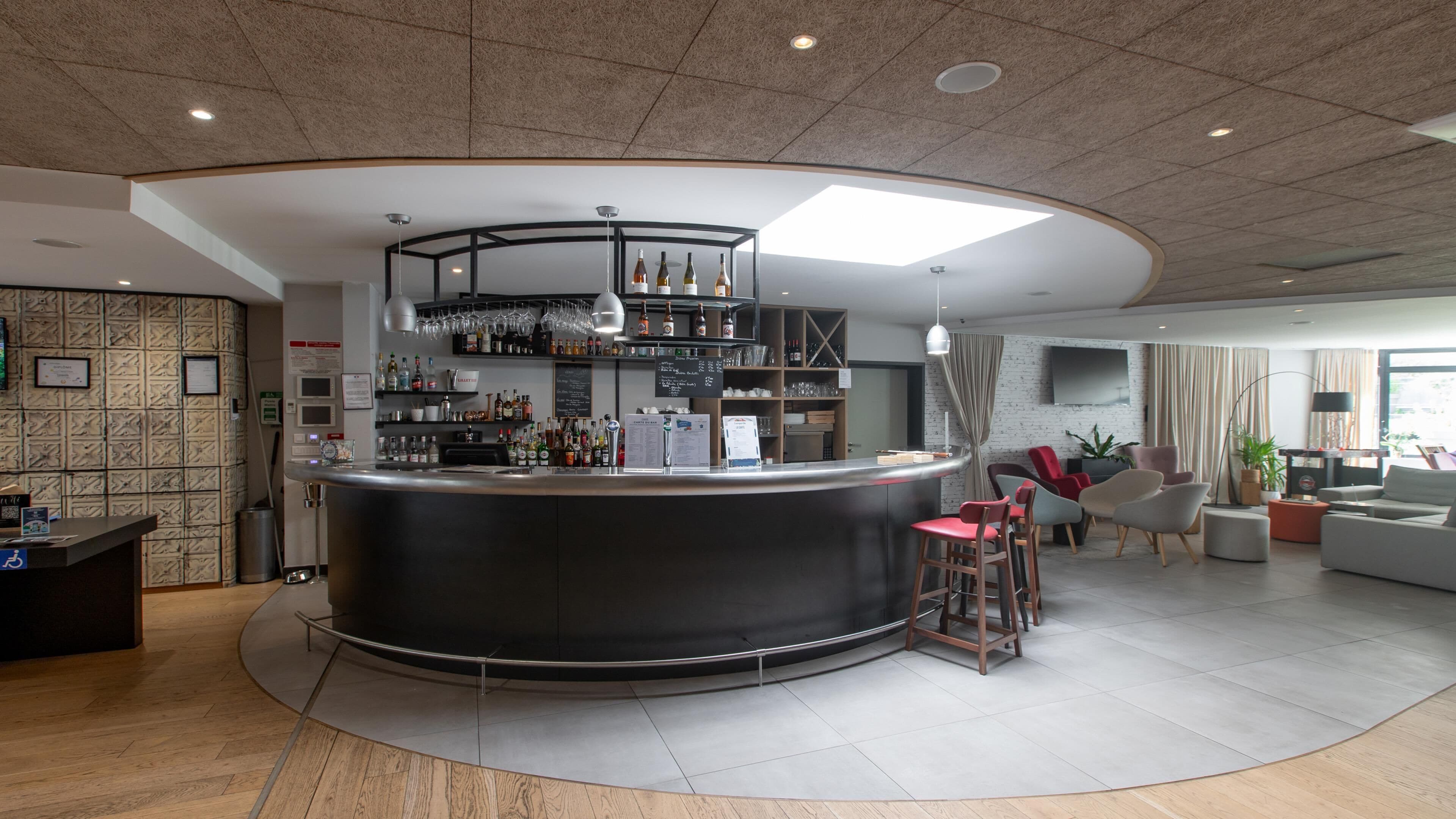 Un área de bar moderna con una barra curva, estantes con botellas y una zona de estar con sillas y un sofá.