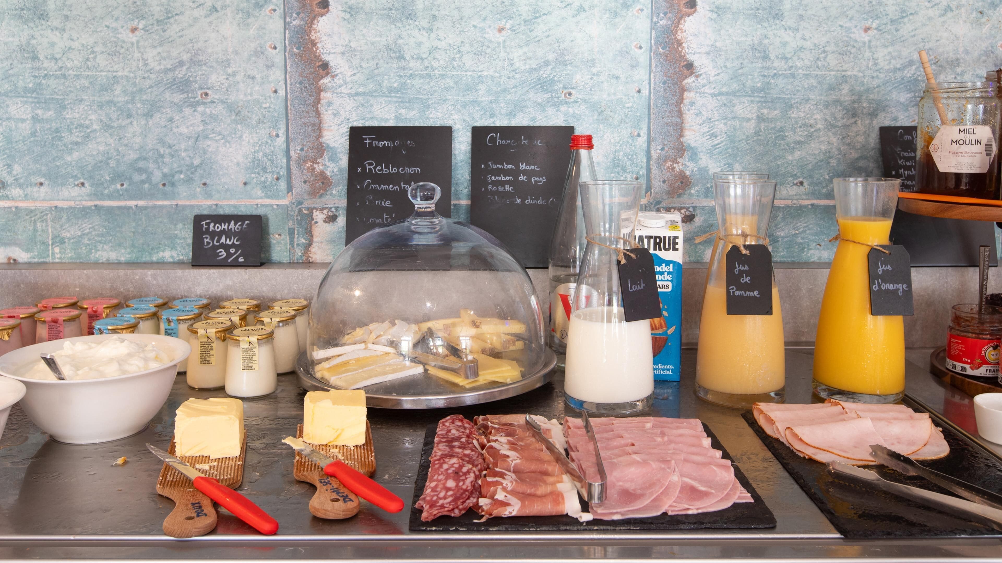 A breakfast buffet with various cheeses, meats, and beverages.