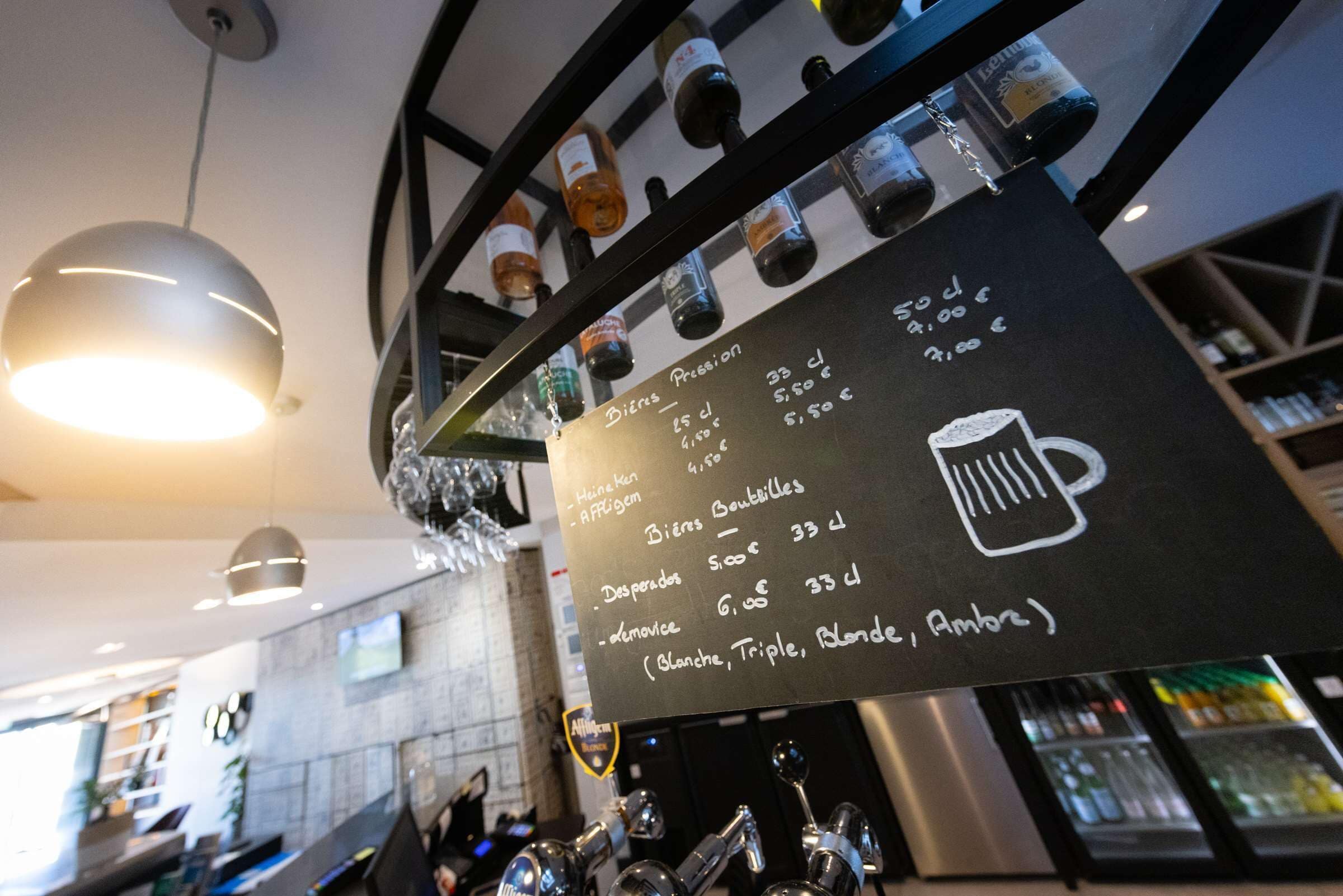 A bar area with a menu board listing beer types and prices, a selection of beer taps, and a hanging light fixture.