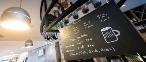 A bar area with a menu board listing beer types and prices, a selection of beer taps, and a hanging light fixture.