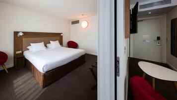 Une chambre d’hôtel avec un lit, une télévision, un bureau et une chaise rouge.
