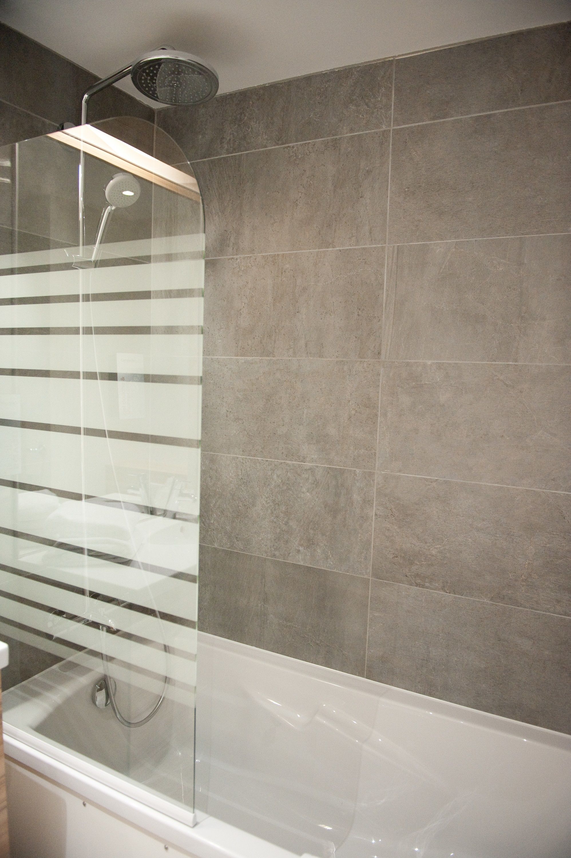 Un baño moderno con ducha envuelta en vidrio, bañera blanca y paredes con azulejos grises.