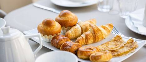 Desayuno con cruasanes, una tetera, tazas y un plato de pasteles sobre una mesa.