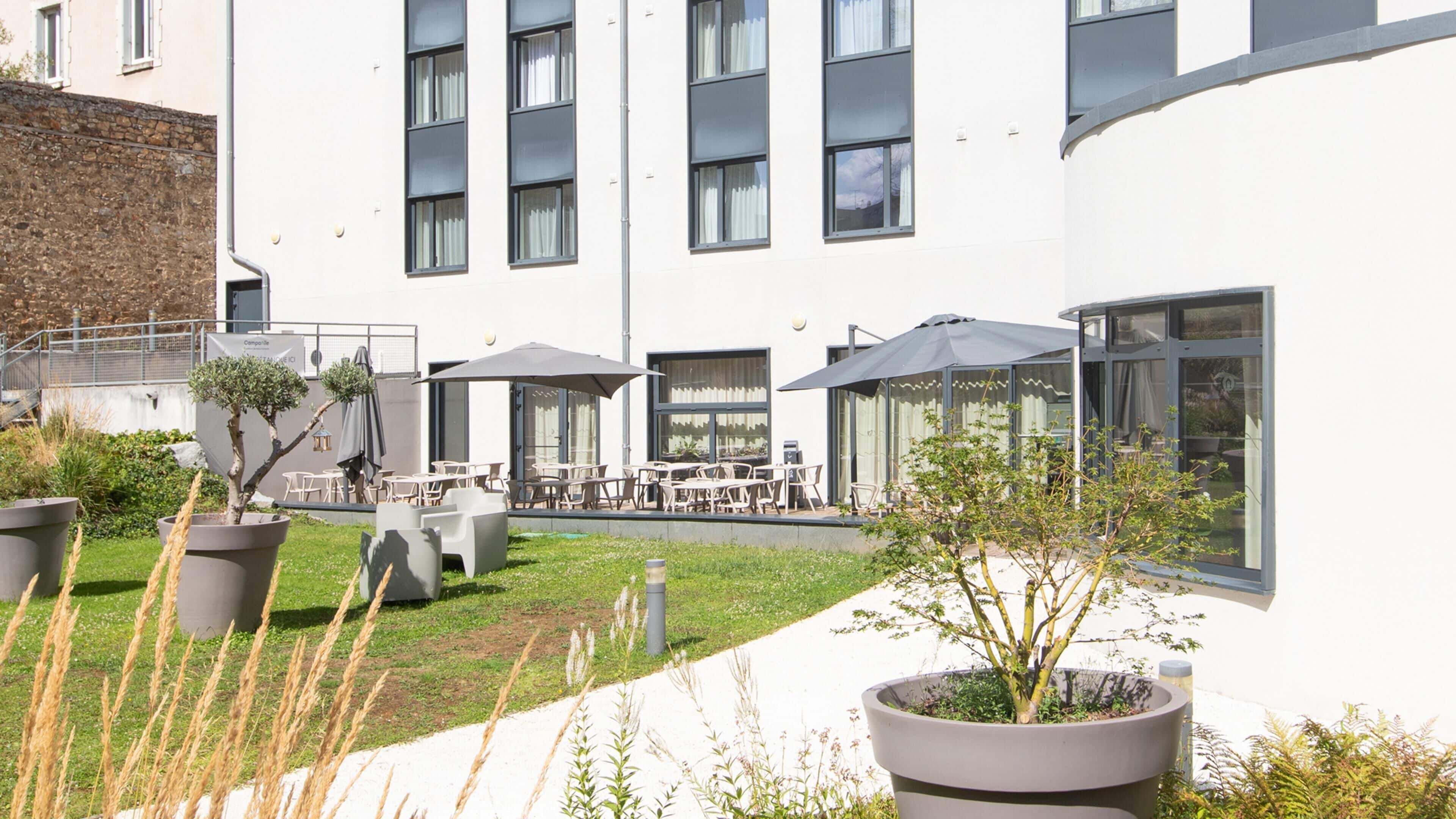 A modern building with a courtyard featuring outdoor seating, potted plants, and a glass-enclosed area.