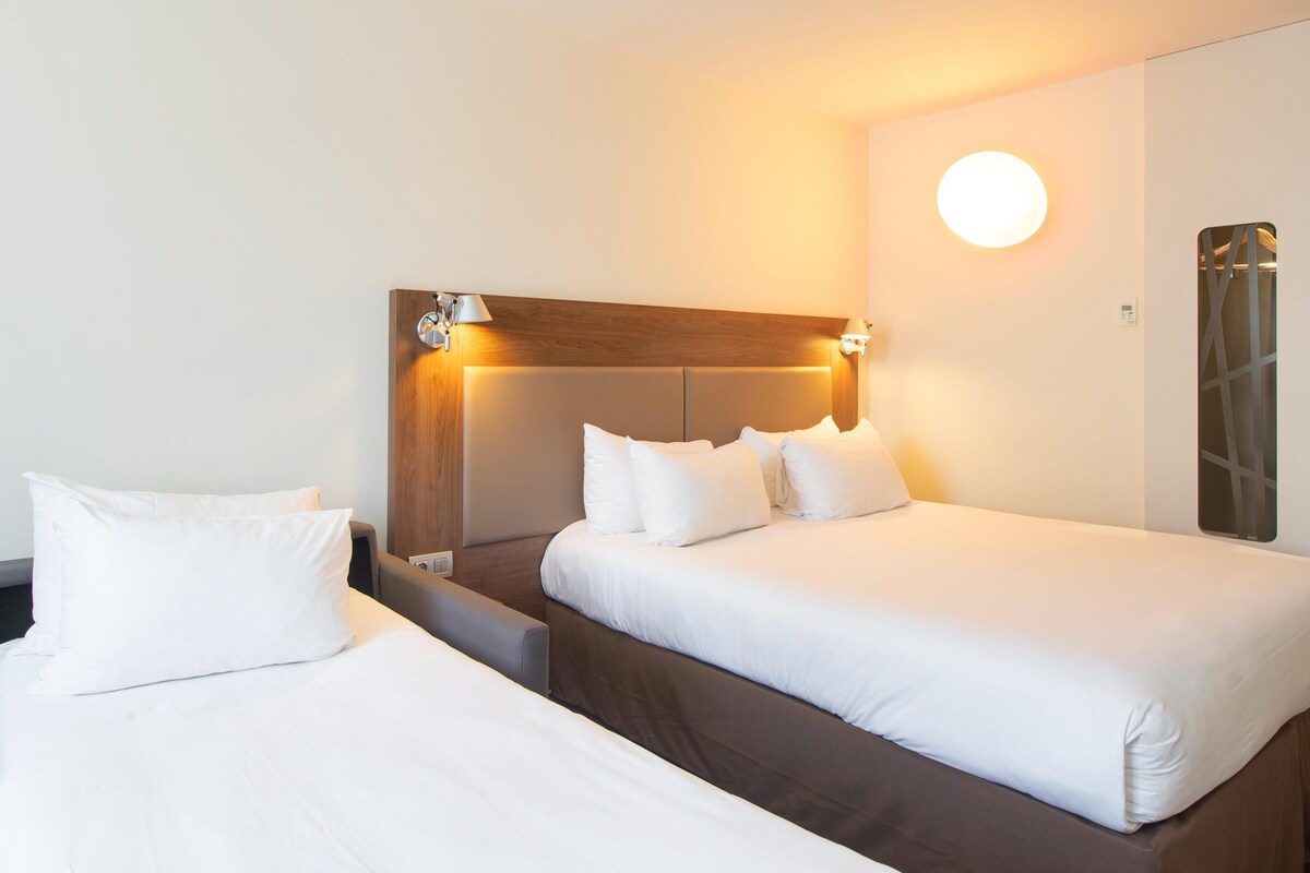 Habitación de hotel con dos camas, un cabecero de madera y una lámpara fijada a la pared.