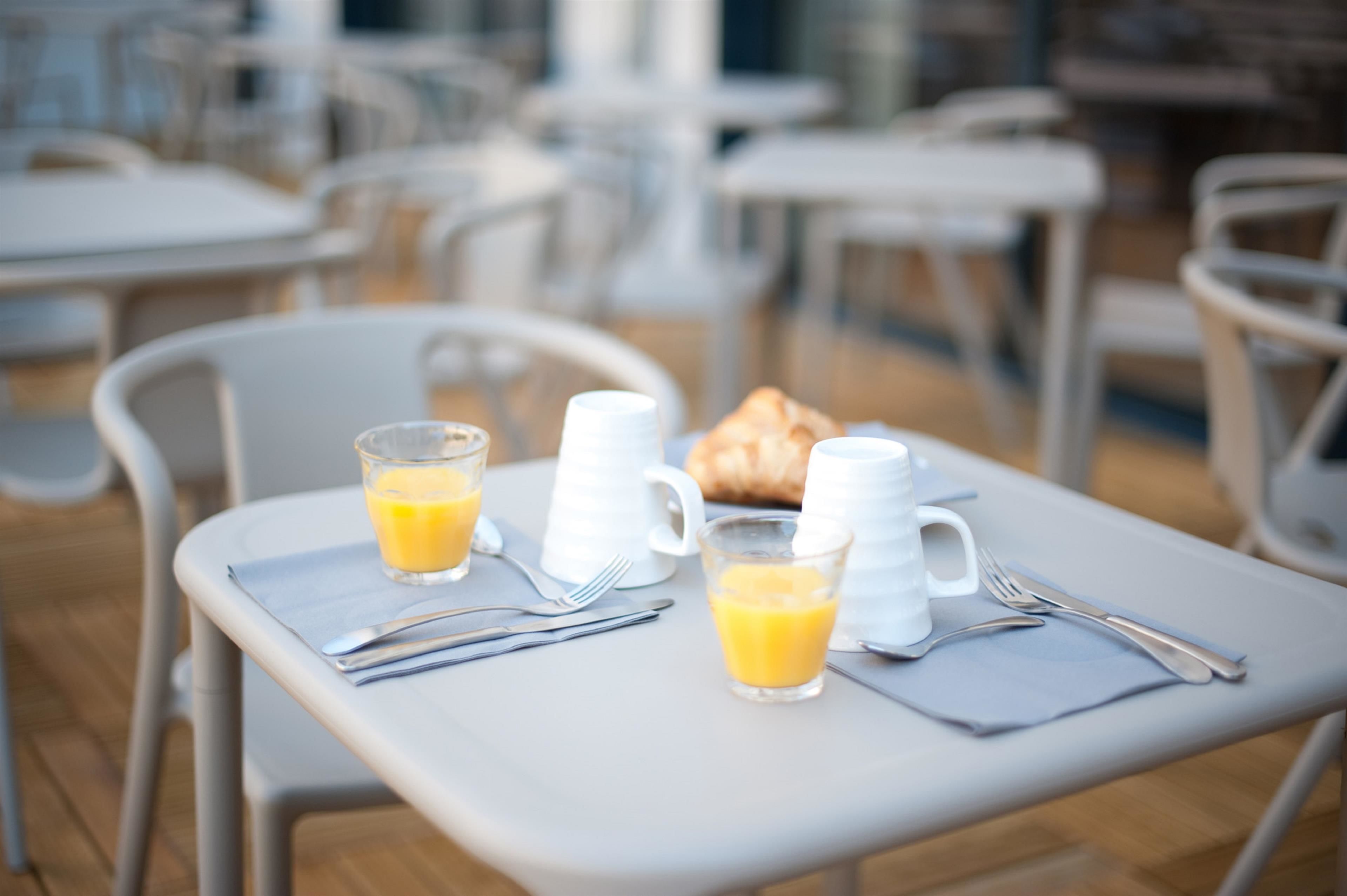 Una mesa de desayuno con un croissant, dos vasos de jugo de naranja y una jarrón blanco.