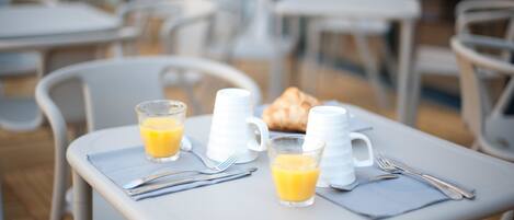 Una mesa de desayuno con un croissant, dos vasos de jugo de naranja y una jarrón blanco.