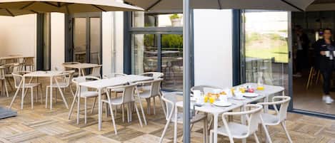 An outdoor patio area with tables and chairs, a large umbrella, and a glass door leading to the interior.