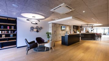 Una moderna zona de recepción con suelo de madera, mostrador de recepción, área de descanso con sillas, estantería y televisor montado en la pared.