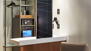 Quarto de hotel moderno com minibar embutido, área de estar com poltrona de couro marrom e uma pequena mesa redonda com um livro.