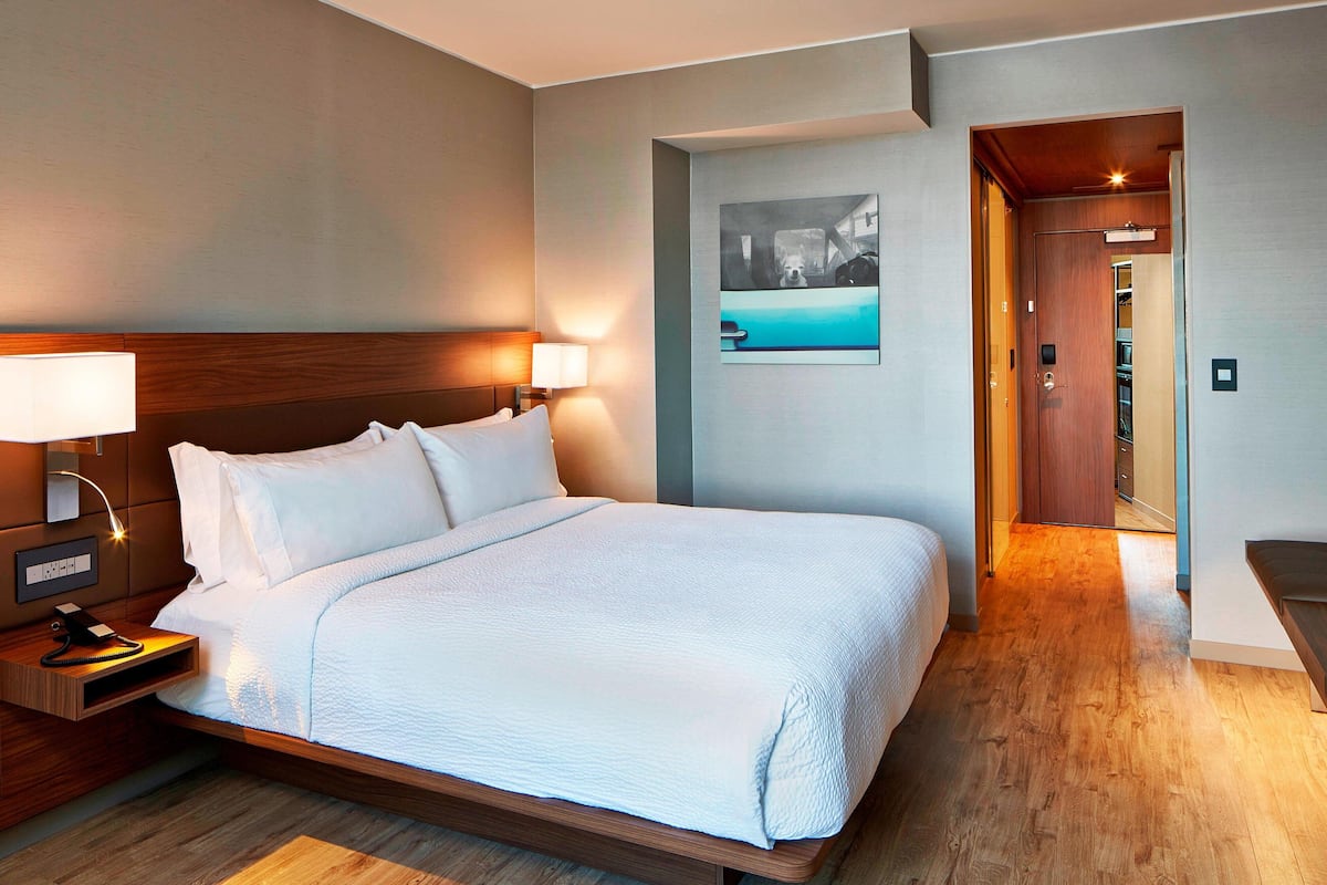 A modern hotel room with a large bed, bedside lamps, a nightstand, and a wooden floor.