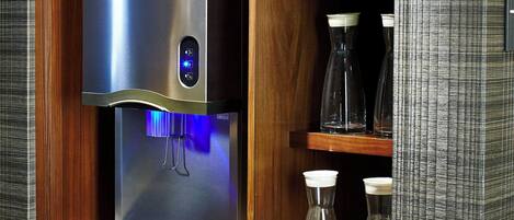 A stainless steel water dispenser with a digital display, placed in a wooden cabinet with a white countertop below.